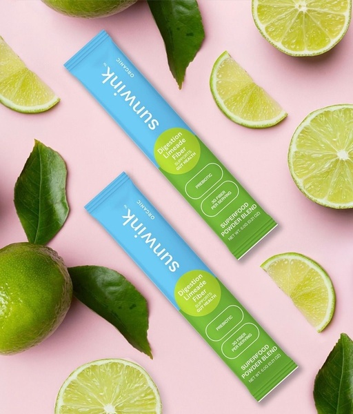 A minimalist, high-contrast creative featuring two product sticks surrounded by fresh limes and leaves on a soft pink background.
